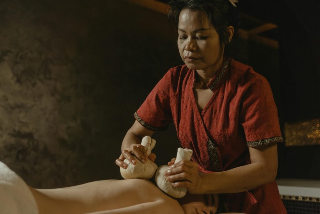 A masseuse performing therapeutic massage using herbal compress on a client for relaxation.